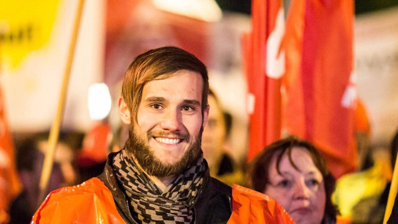 Ein junger Man mit Schal lächelt in die Kamera.