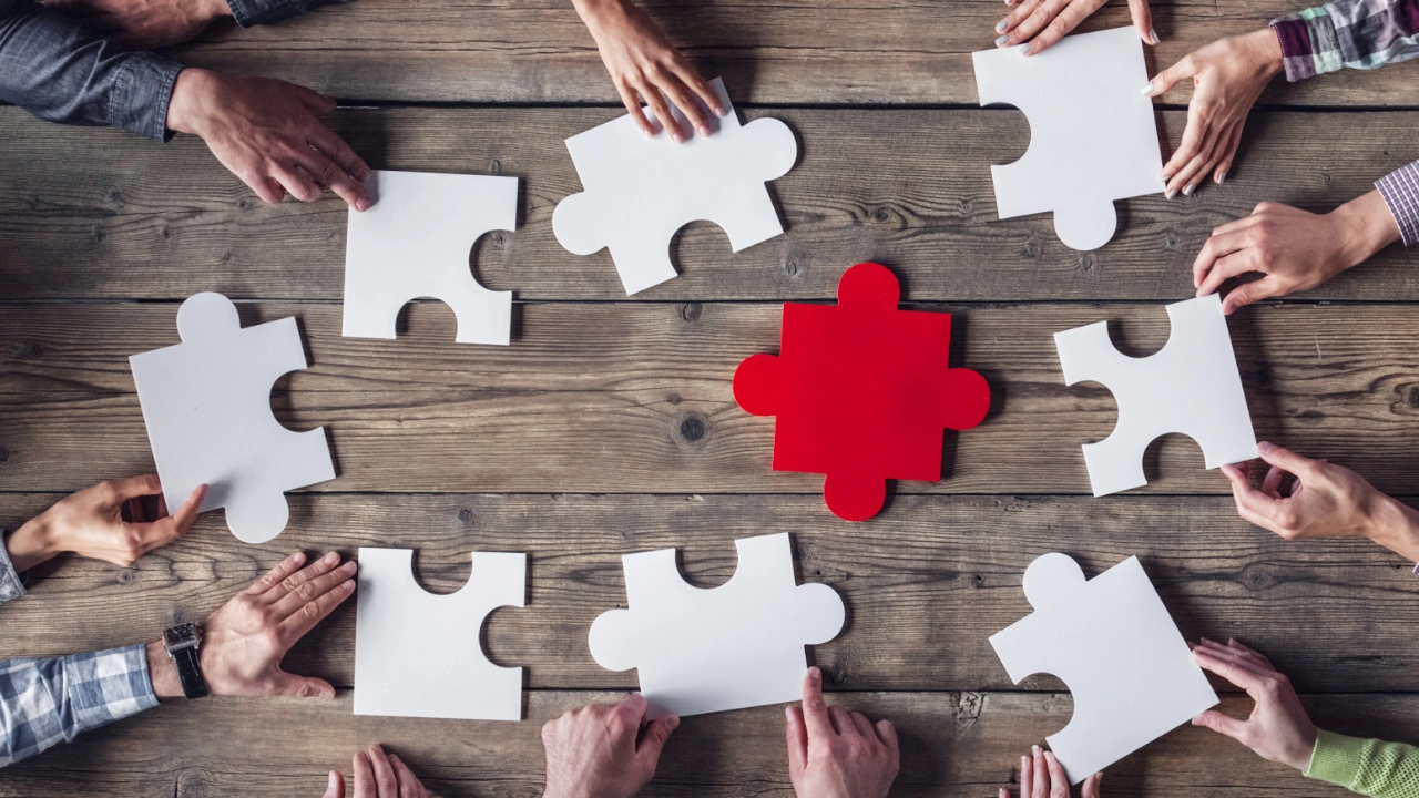 Ein rotes und weiße Puzzleteile auf dem Tisch umrahmt von Händen