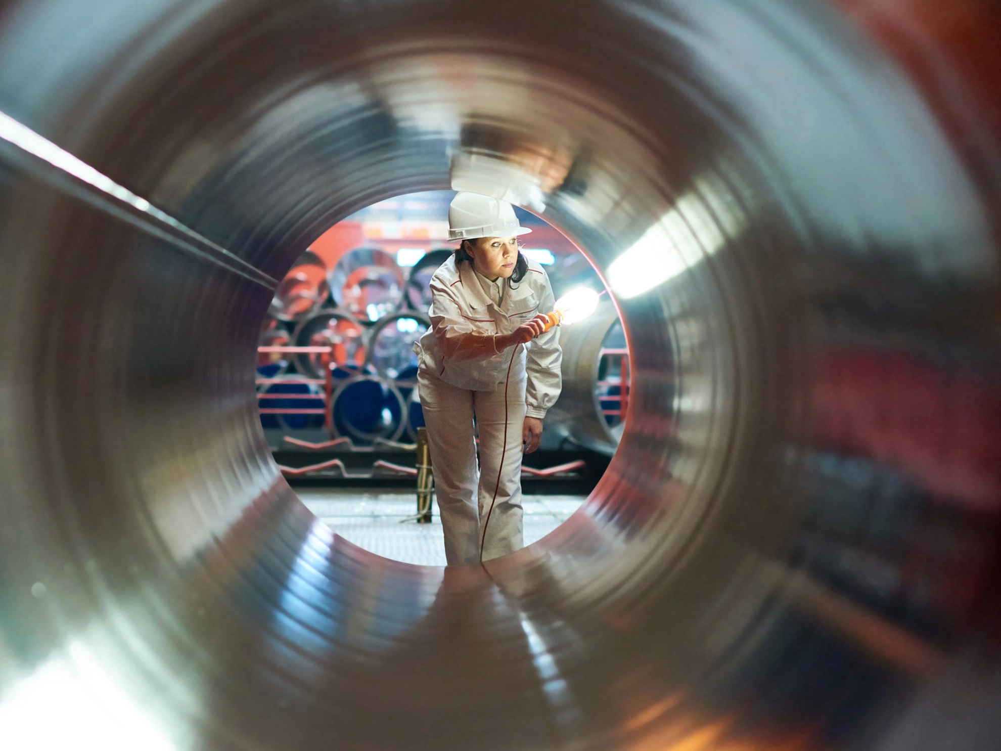 Eine Frau in Arbeitsschutzkleidung leuchtet mit einer Taschenlampe in ein Rohr.