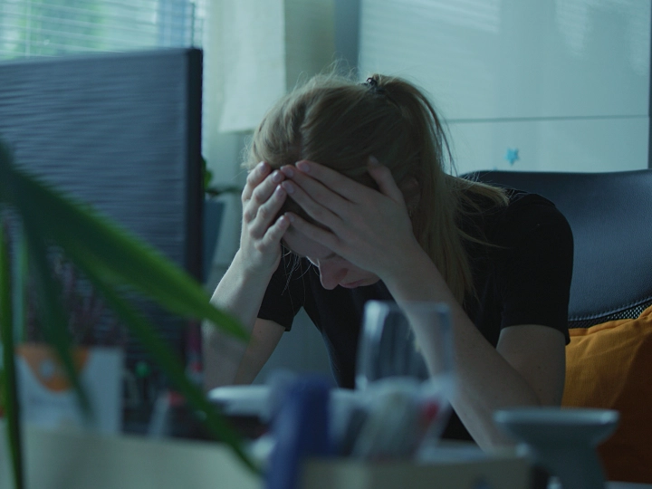 Frau mit gesenkten Kopf an ihrem Schreibtisch im Büro. 