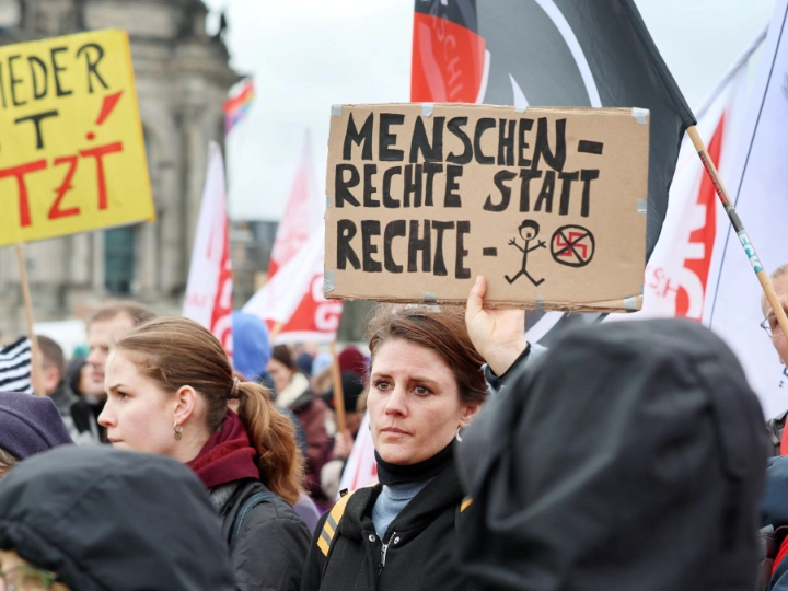Menschenmenge bei einer Demo. Eine Frau hält ein Schild hoch mit der Aufschrift „Menschenrechte statt rechte Menschen“.
