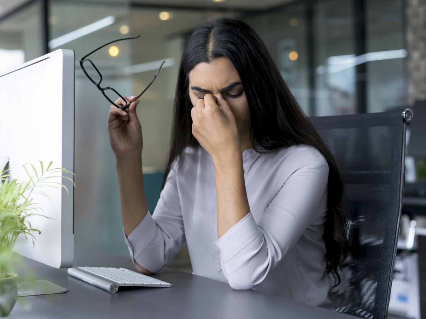 Eine junge Frau reibt sich im Büro aus Übermüdung die Augen